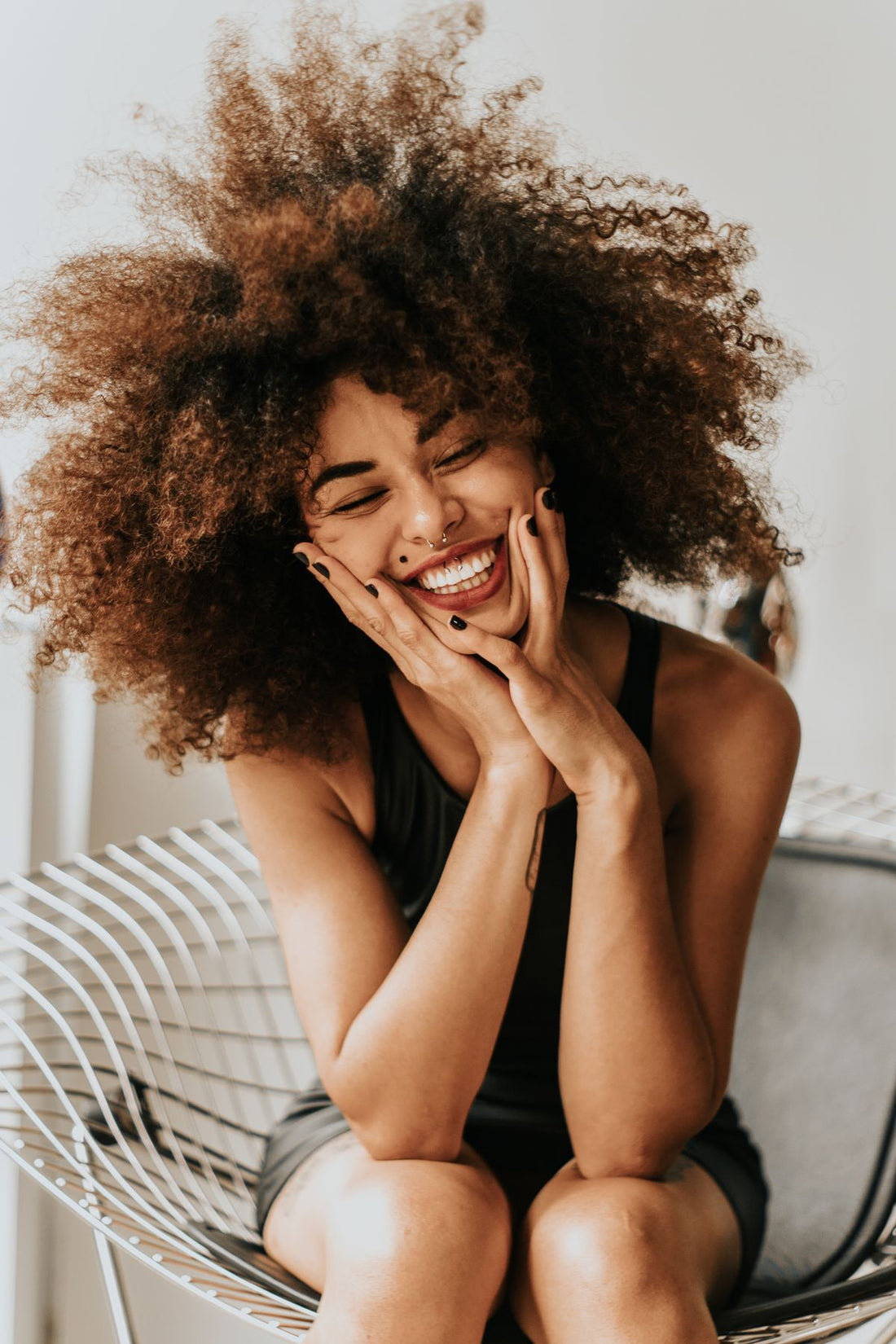 Centered portrait of a woman in a black tank styled with simple face jewelry