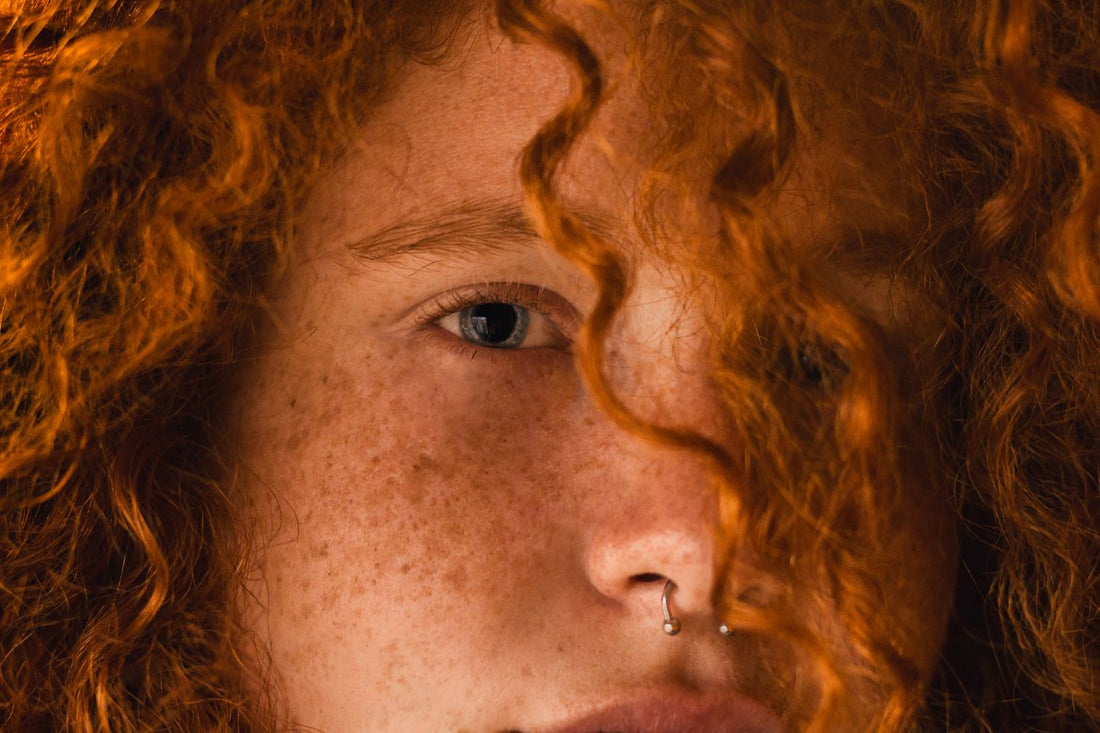 Close-up portrait with red curly hair and nose jewelry in warm color contrast