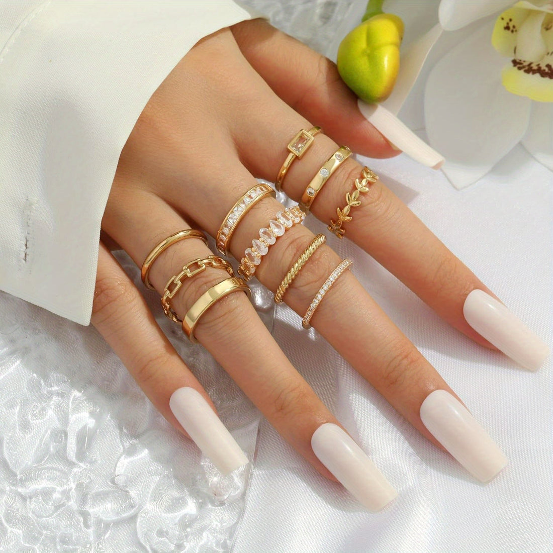 Gold stacking rings styled on a hand with a soft white outfit