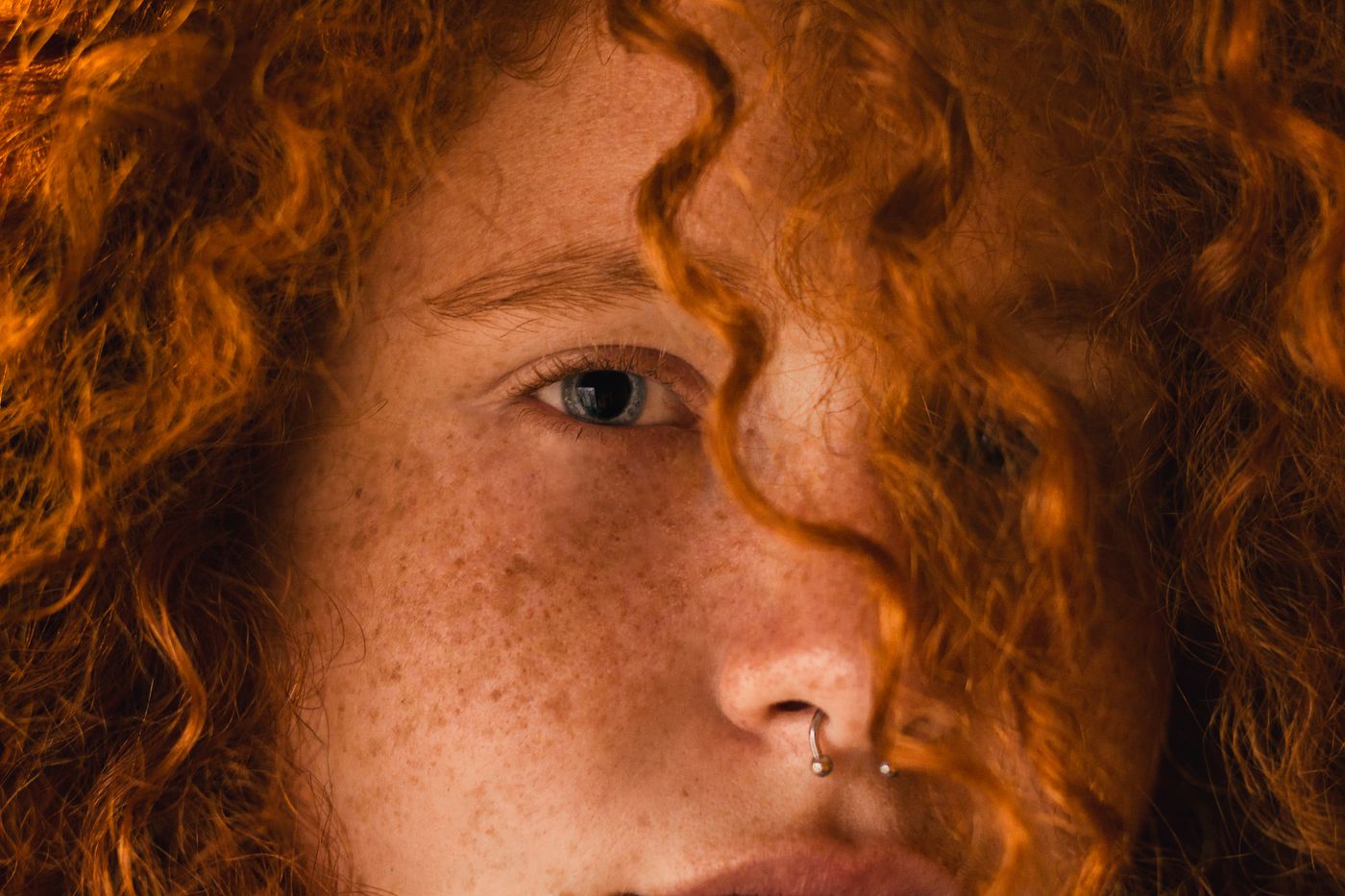 Close portrait of a model with copper curls and a silver nose ring