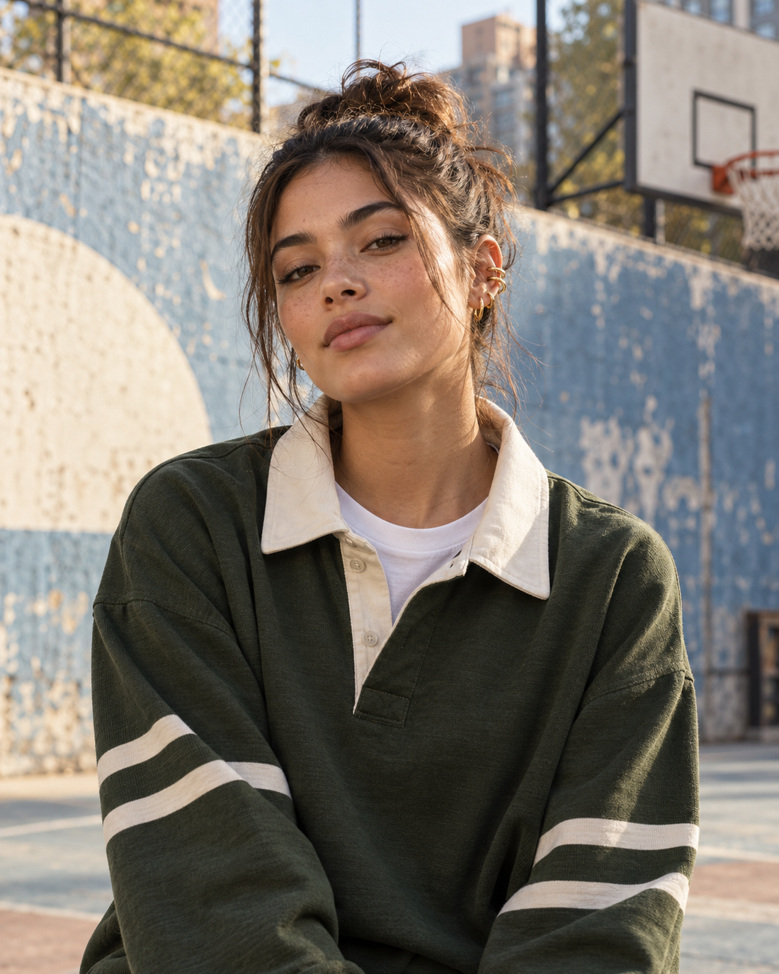 Adult model in a moss-green rugby shirt with gold ear cuffs at an outdoor city basketball court