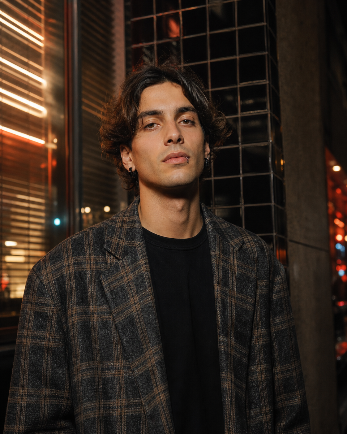 Adult model in a plaid blazer wearing a small black lip ring and dark ear jewelry