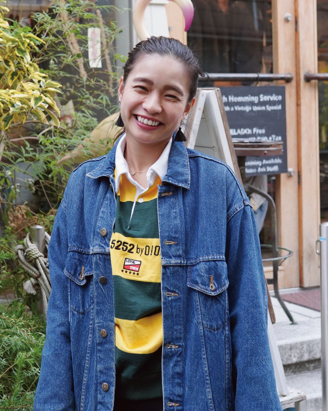 Streetwear model wearing an indigo denim jacket and striped rugby shirt outside a cafe