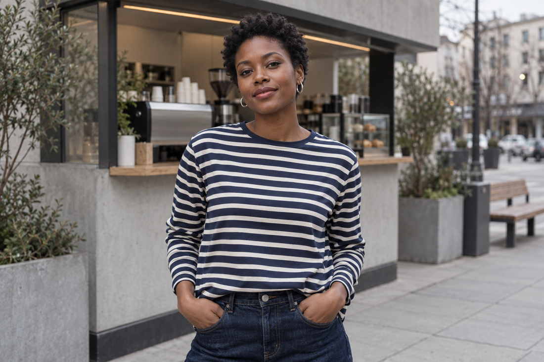 Adult model wearing a navy and ivory striped tee with compact silver ear hoops outside a city coffee kiosk