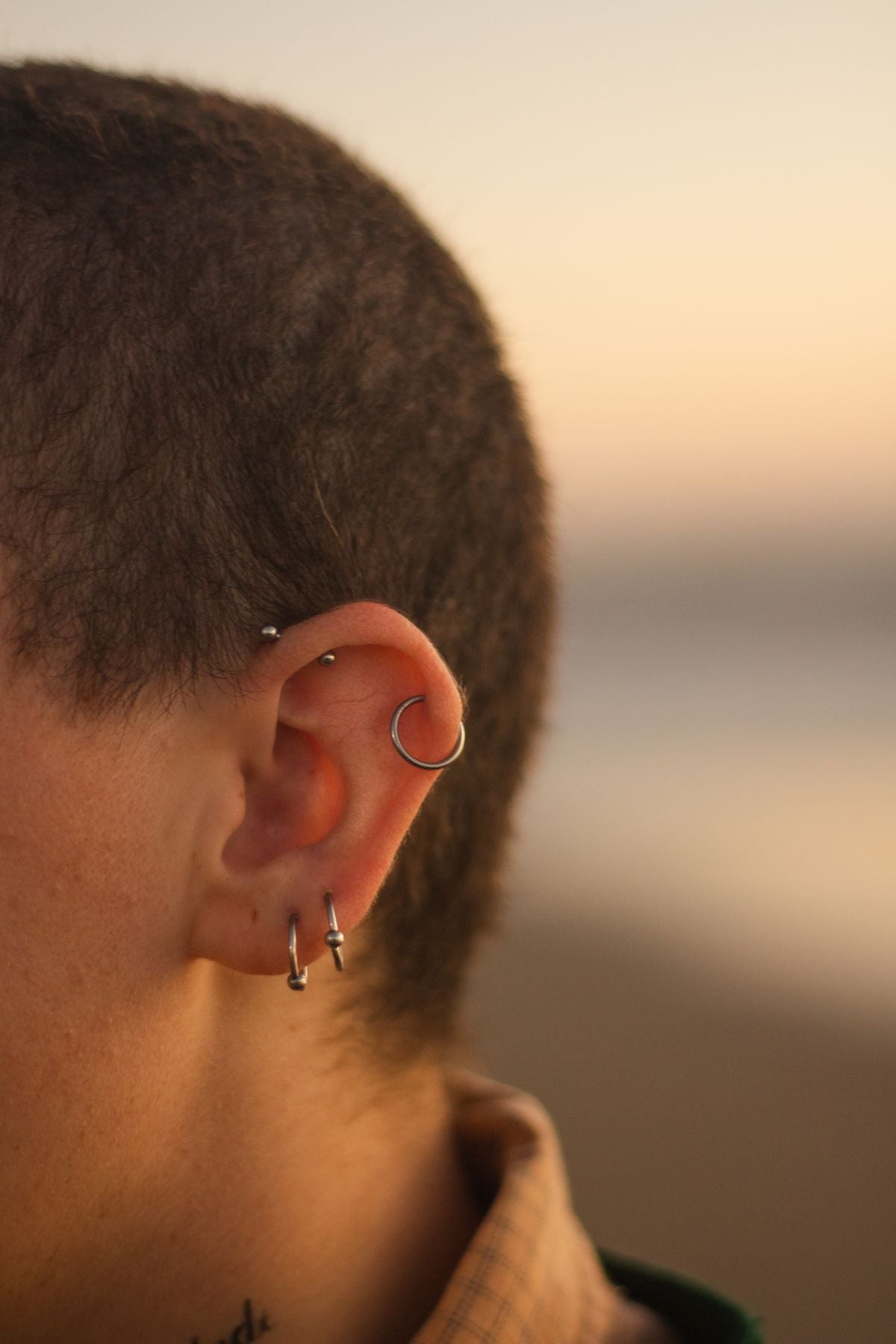 Close-up lifestyle photo of a model wearing multiple ear piercings and hoop jewelry at golden hour