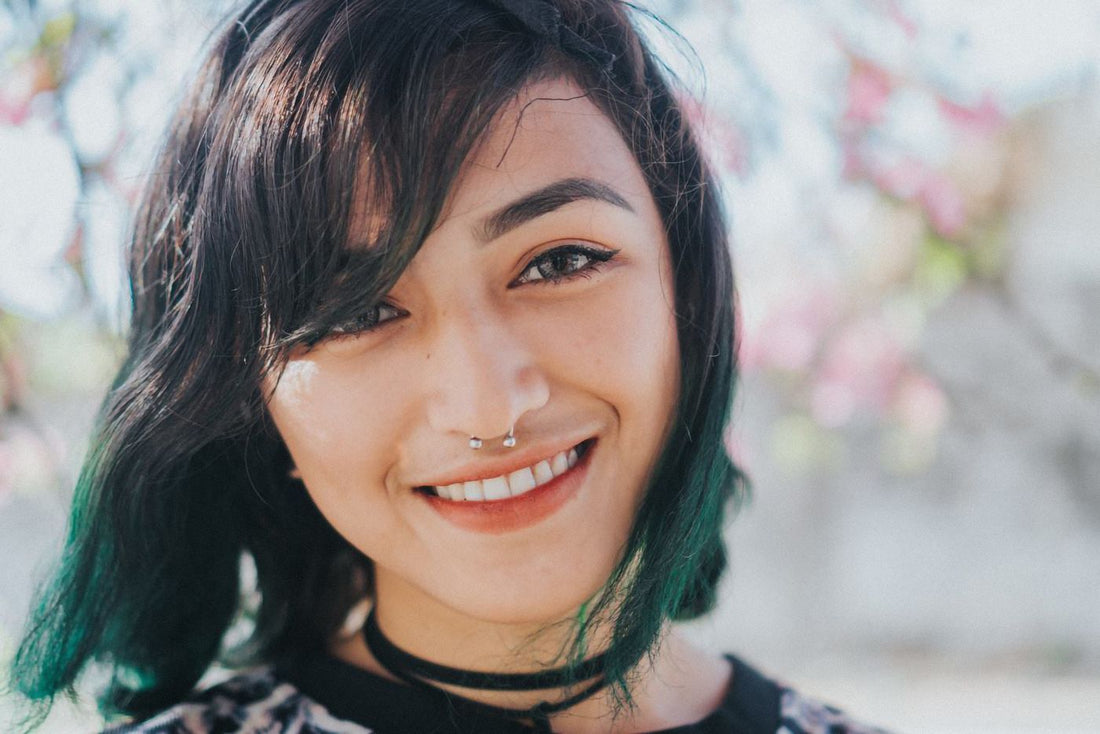 Smiling woman with colorful hair and small nose jewelry in soft outdoor light