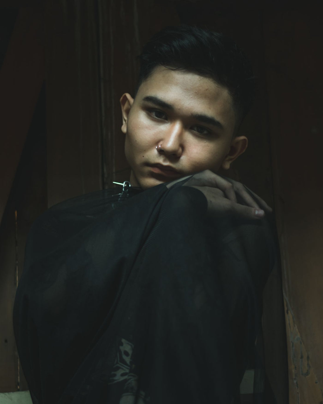 Low-light portrait of a model with nose jewelry and dark streetwear layers