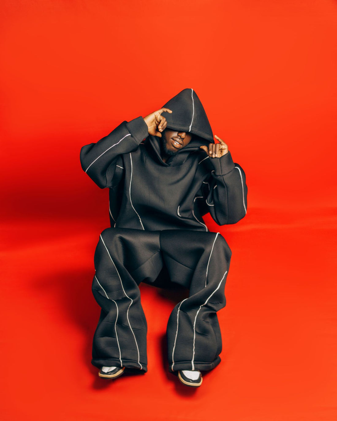 Model in an oversized black hoodie against a bold red background